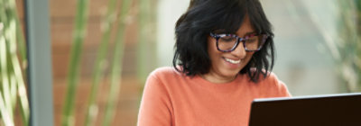 Una persona che indossa occhiali e una felpa arancione sorride mentre guarda il portatile. 