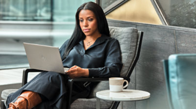 Person sits in a comfortable armchair looking at a laptop.