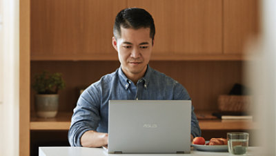 Person sits at their kitchen counter working on a laptop.