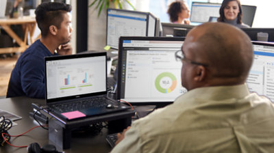 Fotografija nekoliko osoba koje rade u uredu i gledaju velike stolne monitore za svojim radnim stolovima