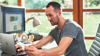 Person in a home office sits at a desk and uses a laptop connected to an external display monitor.