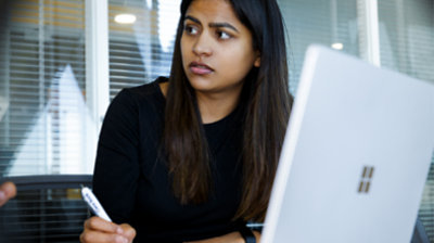 Fotografija osobe koja nešto zapisuje u bilježnicu dok radi na prijenosnom računalu Surface