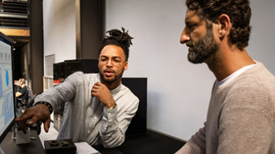 Fotografija dviju osoba koje gledaju informacije na velikom stolnom monitoru i razgovaraju