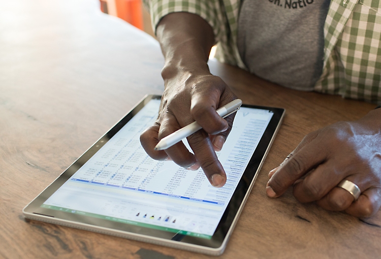 Close-up of a person’s hands working on an Excel spreadsheet on a tablet screen