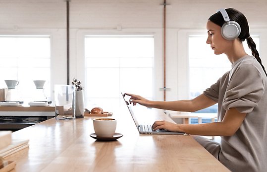 Photograph of person wearing headphones seated at a counter touching the screen of a laptop