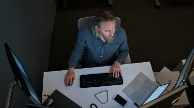 A bird’s eye view of a person working at their desk with multiple screens and a laptop