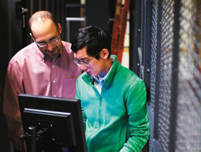 2 人の人が大型のデスクトップ モニターを見下ろしています。