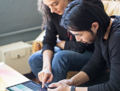 Two people sitting on a couch, one is using a tablet device, one is using a mobile device