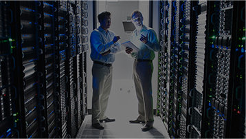 Two people standing in a server room, one is holding a tablet device