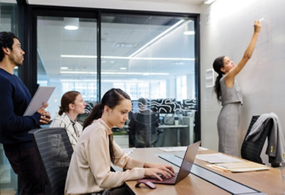 Four people in a conference room, with one person writing on a whiteboard