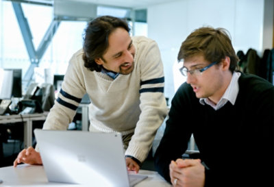 Two people in an office, conferring over a device at a desk