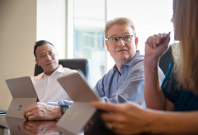 Tres empleados sentados en una sala de juntas sosteniendo tabletas y discutiendo.