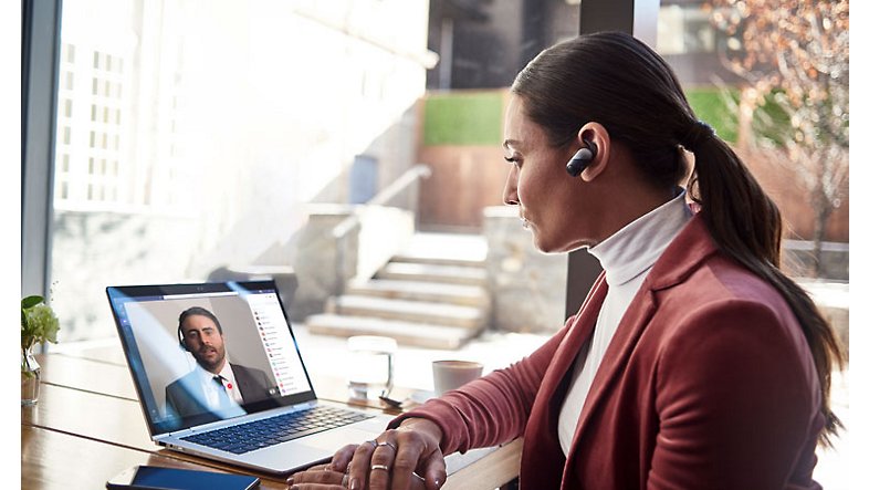A person wearing a wireless in-ear device sitting at their desk participating in a video chat with one other participant on their laptop.