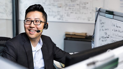 Person som sitter foran store stasjonære skjermer med et headset og smiler og ser til den ene siden.