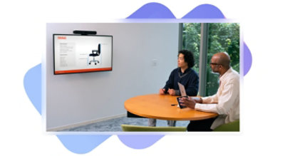 Zwei männliche Personen in einem kleinen Konferenzraum mit einem Poly-System für Microsoft Teams-Räume und einem Android-Touchdisplay. Großes integriertes Gerät und wandmontiertes Display mit Bildschirmfreigabe und einem Surface-Laptop