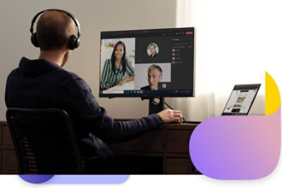 Man sitting at a desk in front of a computer with Teams meetings on display, wearing headphones. A Teams display is on the desk.