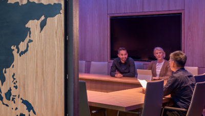 View from office doorway of three people sitting at a conference table engaged in conversation