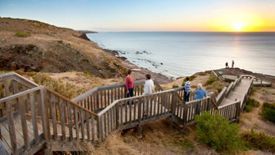 Menschen, die bei Sonnenuntergang auf einer Holzpromenade in den Hügeln entlang des südaustralischen Ozeans spazieren gehen