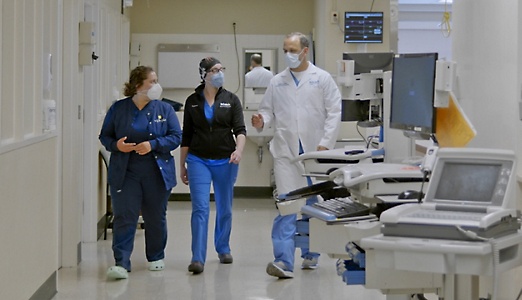 Three healthcare professionals walking down a hallway filled with medical equipment in a hospital.