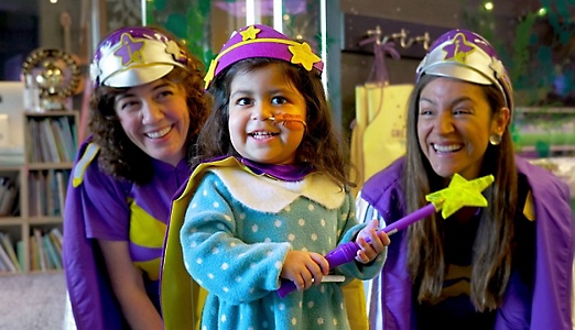 A child with a nasal tube dressed up as a wizard with a crown and wand posing with two adults dressed in costume to match the child.