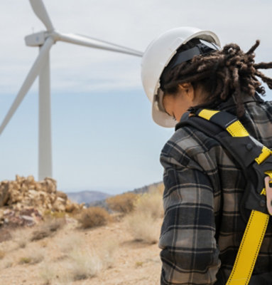 A person wearing protective gear and standing in a field with wind turbines.