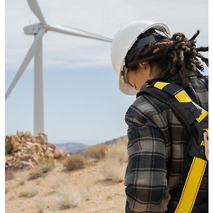 A person wearing protective gear and standing in a field with wind turbines