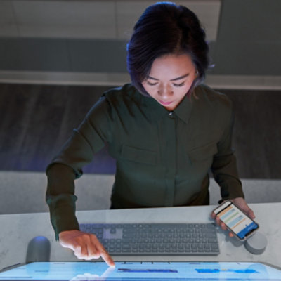 Draufsicht auf eine Person, die einen großen Touchscreen nutzt und ein Mobiltelefon hält.