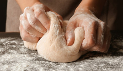 Zwei Hände kneten Teig auf einem Tisch.