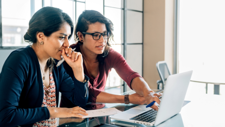 Two people sitting at a desk working together on a laptop.