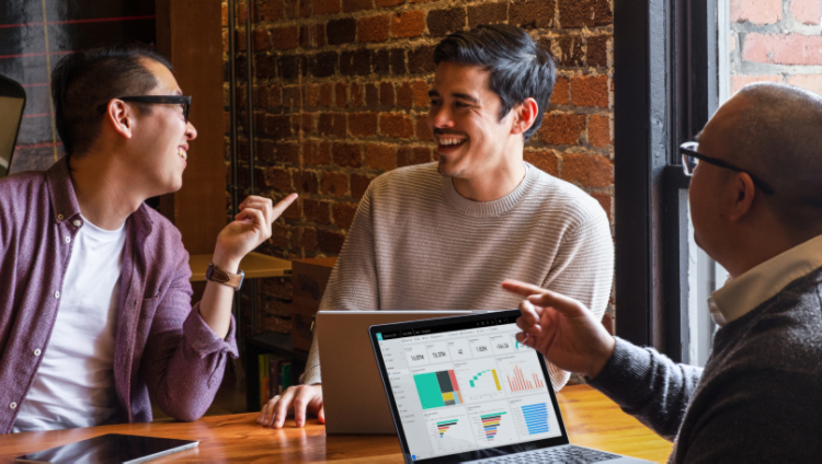 Three people seated around a table with laptops having a conversation.