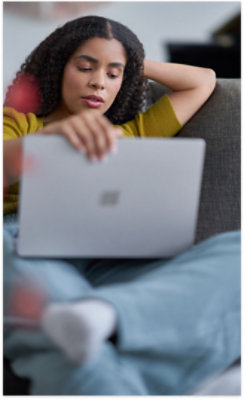 Person with curly hair sitting on a couch, using a laptop. They are wearing a yellow top and blue jeans.