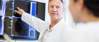 A man in a white coat pointing at a computer screen.