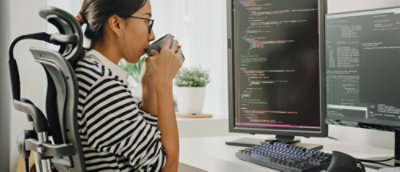 Person sitting at a desk with a coffee cup, working on a computer with multiple lines of code on the screen.