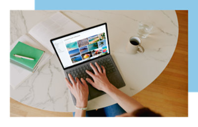 Une personne travaillant sur un ordinateur portable avec une galerie de photos à l’écran, un carnet de notes et une tasse de café sur une table en marbre.