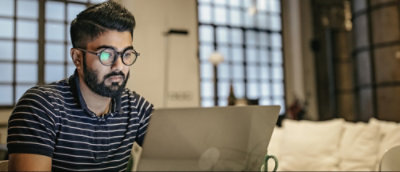 Egy szemüveget és csíkos inget viselő személy egy laptopra koncentrál egy nagy ablakokkal rendelkező modern helyiségben.