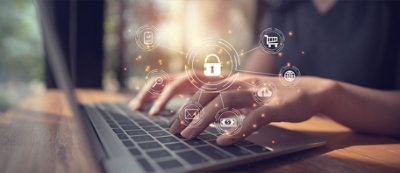 Una persona digita sulla tastiera del portatile, con icone digitali di lucchetti sovrapposti che simboleggiano la cybersecurity.