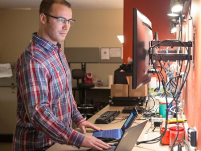 一位戴眼鏡、穿著格子襯衫的男士站在電腦前。