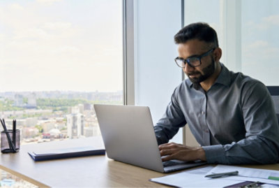 Person working on a laptop at an office desk with a cityscape visible through the window.