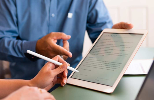 A seller holding a tablet with a short contract on display, while a customer is about to sign on it.