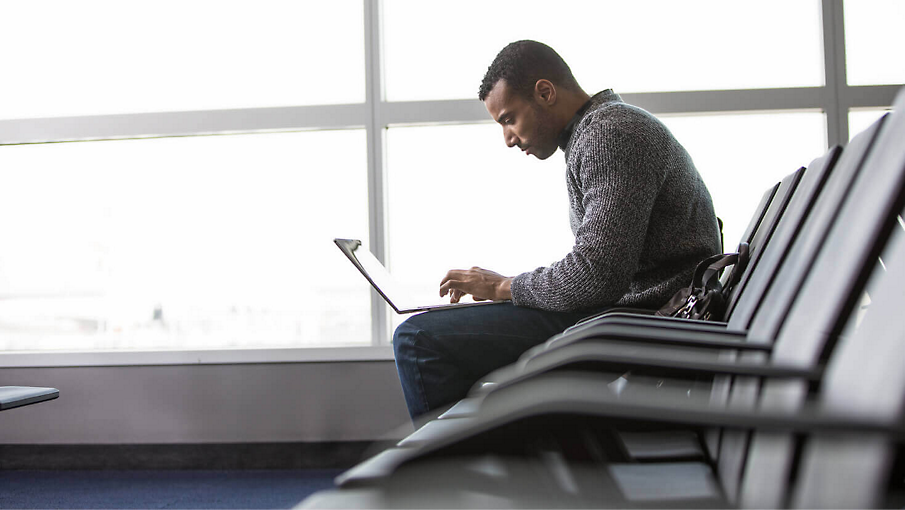 Osoba pracující na letišti na přenosném počítači.