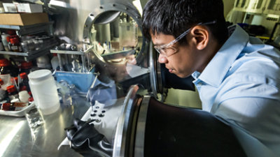 A person in protective gloves and safety glasses works with equipment inside a lab