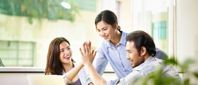 Three people in a bright office high-five and smile, engaged in a moment of teamwork.