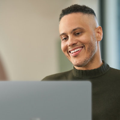 Person with a close-cropped haircut and a beard smiles while looking at a laptop screen.