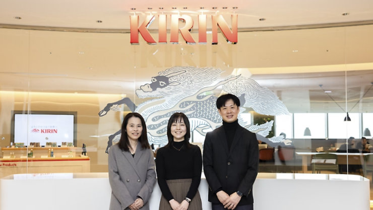KIRINの企業ロゴと麒麟の壁画を背景に、オフィスロビーで笑顔の3人のプロフェッショナル。