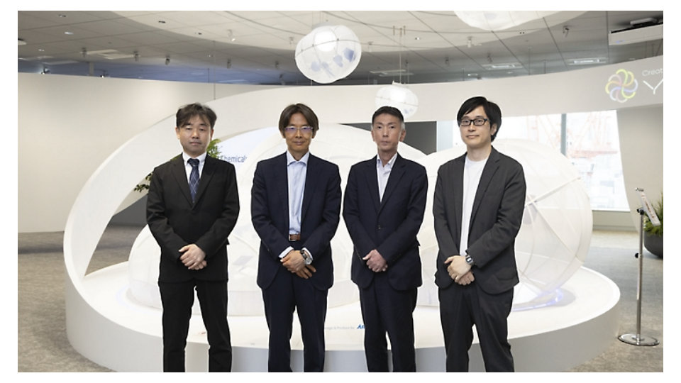 曲線的な白い展示スペースのあるショールームに並んで立つ、ビジネススーツ姿の4人