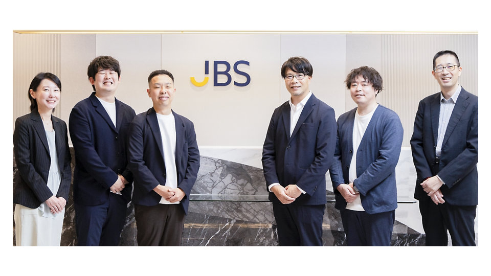 JBSのロゴが掲げられた受付エリアの前に、6名が並んで立っている様子。