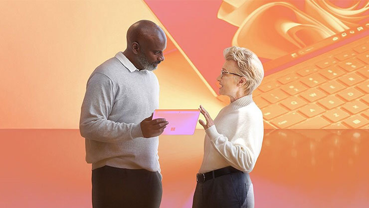 Zwei Personen betrachten ein Tablet, im Hintergrund ein Laptop mit Windows-Logo. Warme Orange- und Rosatöne.