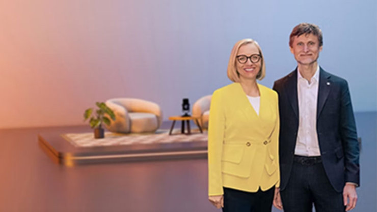 Zwei Personen in Business-Kleidung vor einem stilisierten Hintergrund mit Möbeln.