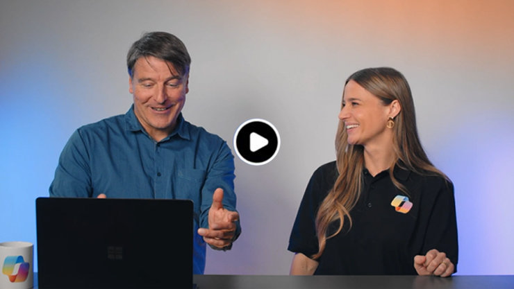 Ein Mann und eine Frau stehen nebeneinander. Der Mann trägt ein blaues Hemd und bedient einen Laptop. Die Frau trägt ein schwarzes Poloshirt. Sie schaut ihn an und lächelt. Der Hintergrund ist in blau-orangefarbenem Licht gehalten.