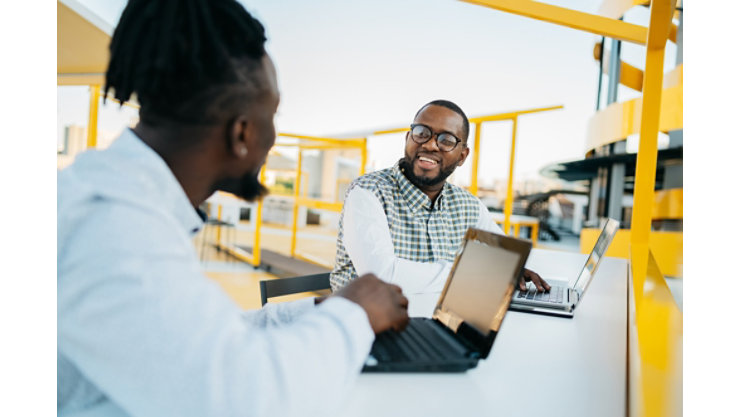 Two men work together on laptops in outdoor workspace.